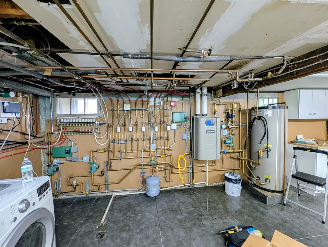 Tankless water heater and hot water storage tank in basement boiler room